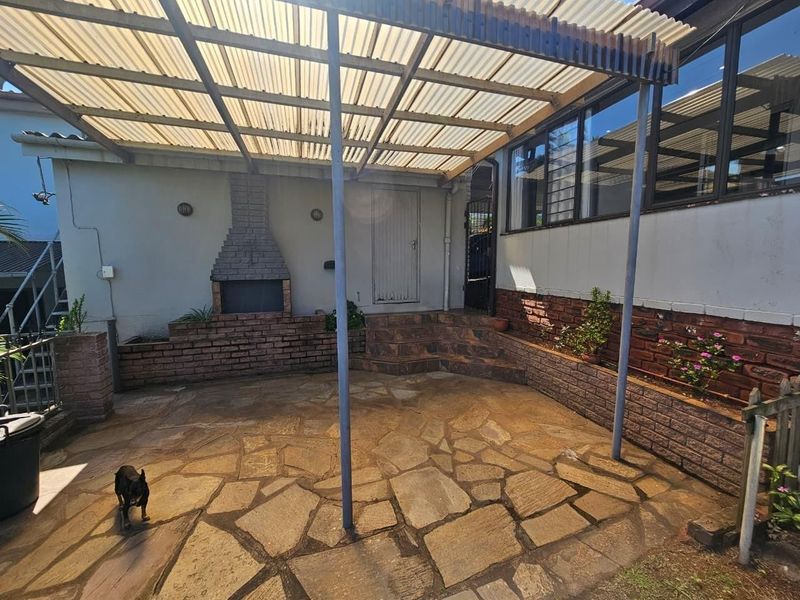 Covered outdoor patio area featuring flagstone paving, a built-in brick fireplace, and a corrugated roof structure, ideal for outdoor entertaining.
