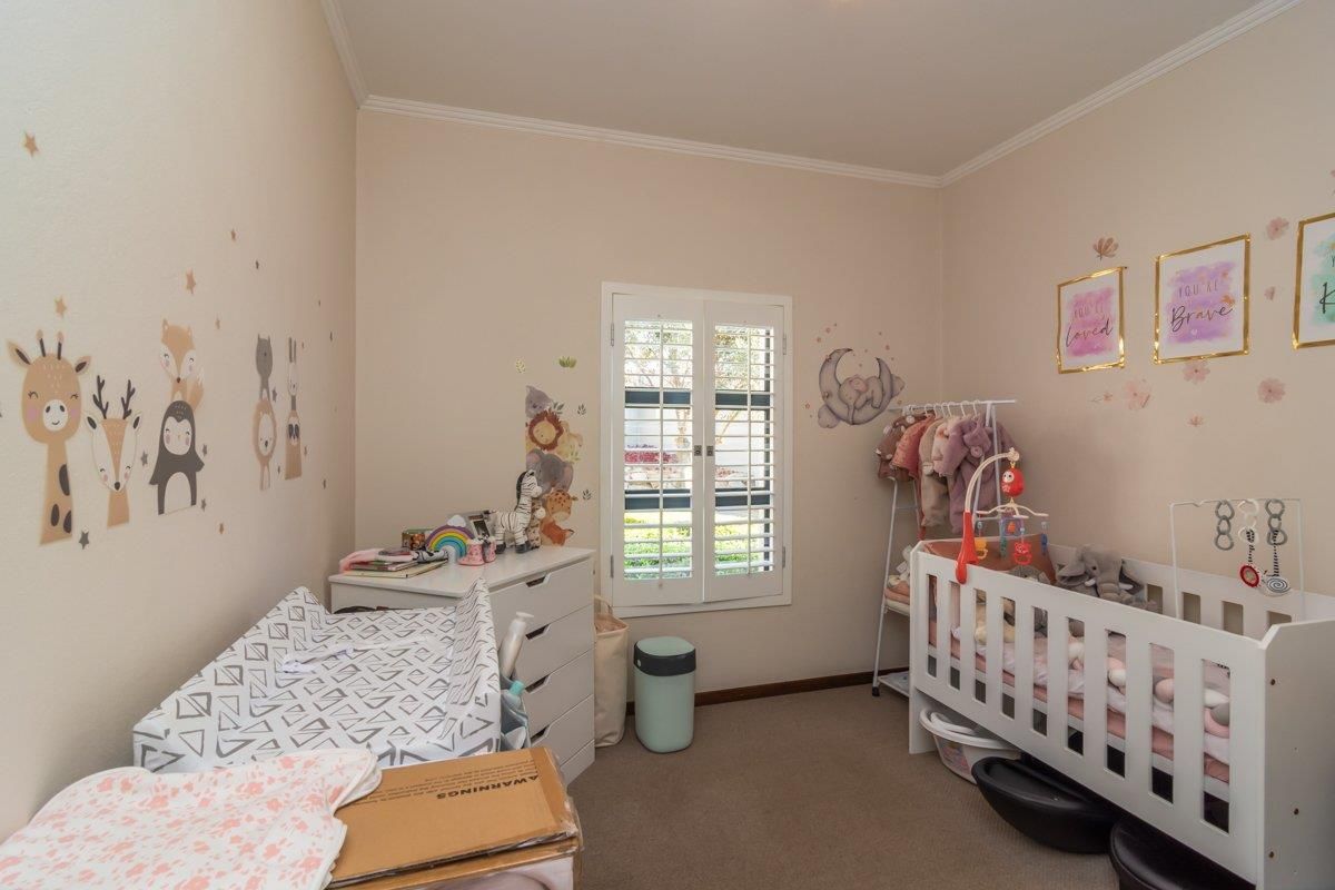A well-maintained bedroom featuring neutral carpeting, crown molding, and white plantation shutters, providing a bright and functional space.