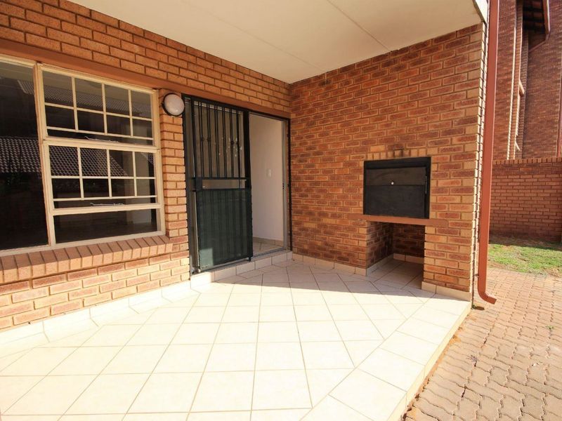 Covered patio area featuring tiled flooring, a built-in brick braai, and a security gate providing access to the apartment interior.
