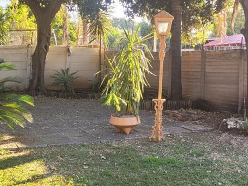 A private garden area featuring a lawn, mature trees, a paved patio section, and a precast concrete boundary wall.