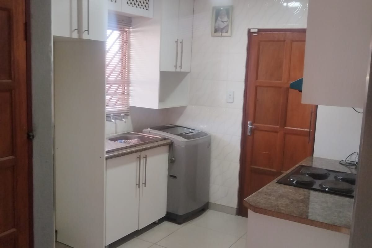 Compact kitchen featuring white cabinetry, laminate countertops, an integrated electric hob, and tiled flooring with dedicated space for laundry appliances.