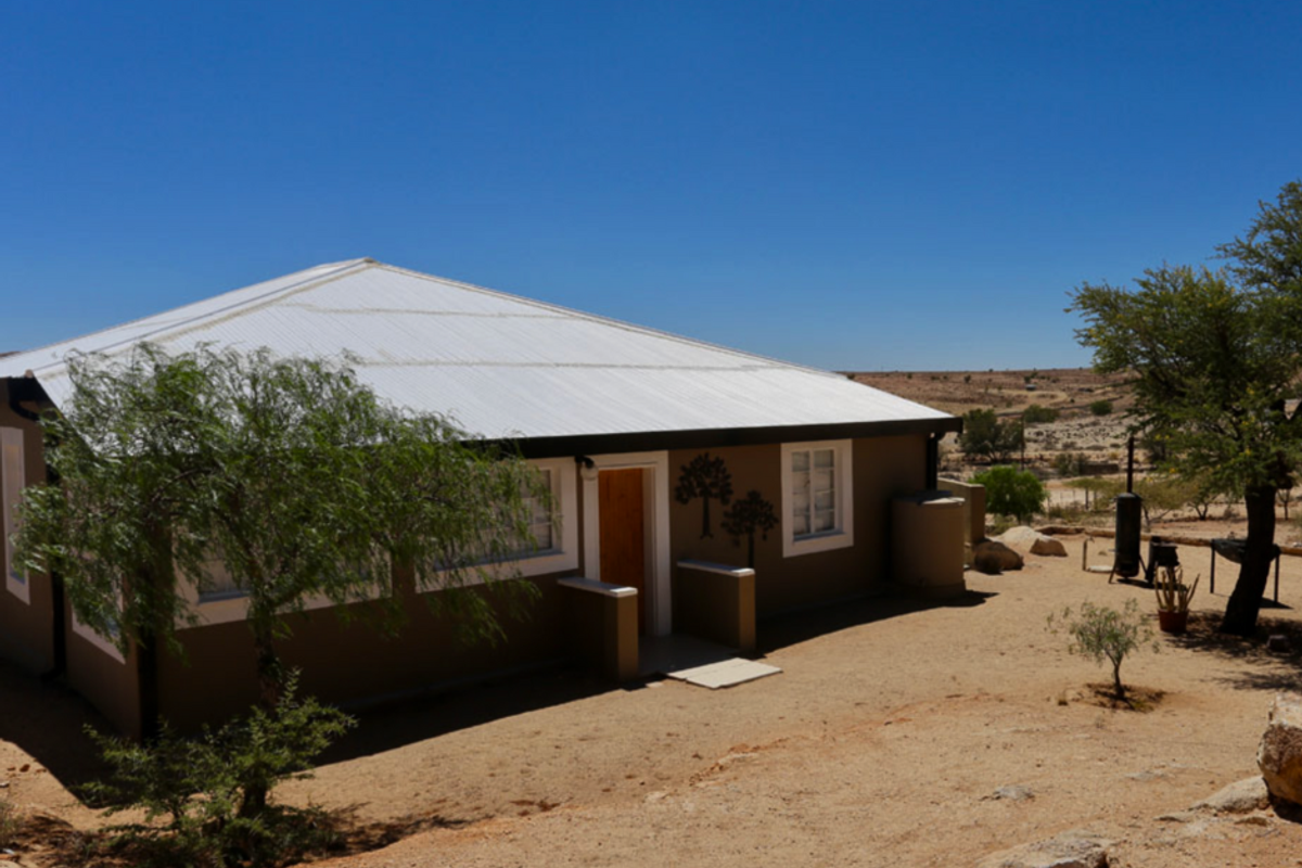 A view of the exterior rear of the hotel building, featuring a corrugated metal roof and a natural, arid landscape setting.