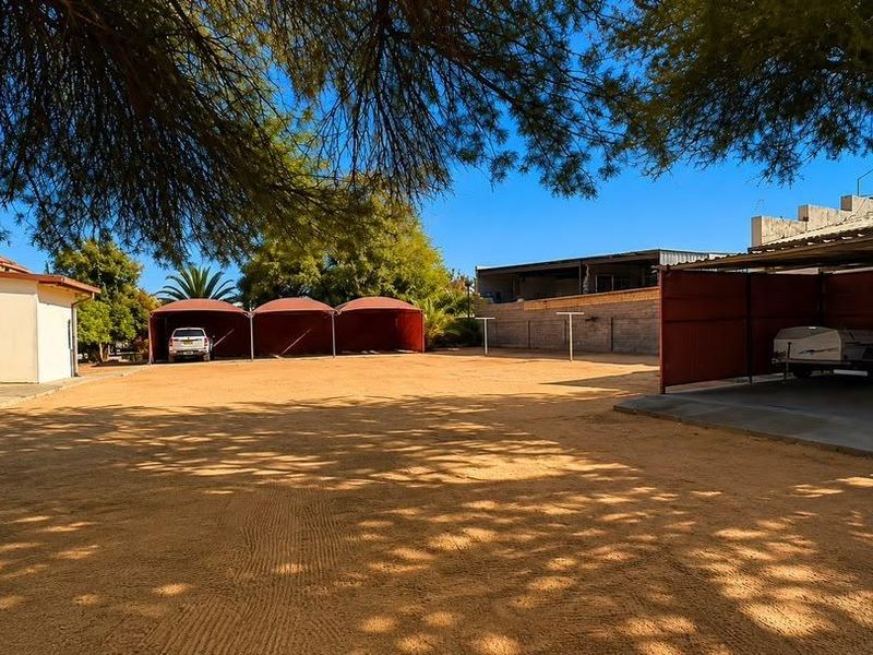 Spacious rear yard featuring multiple shade cloth carports, a concrete parking area, and perimeter boundary walls.