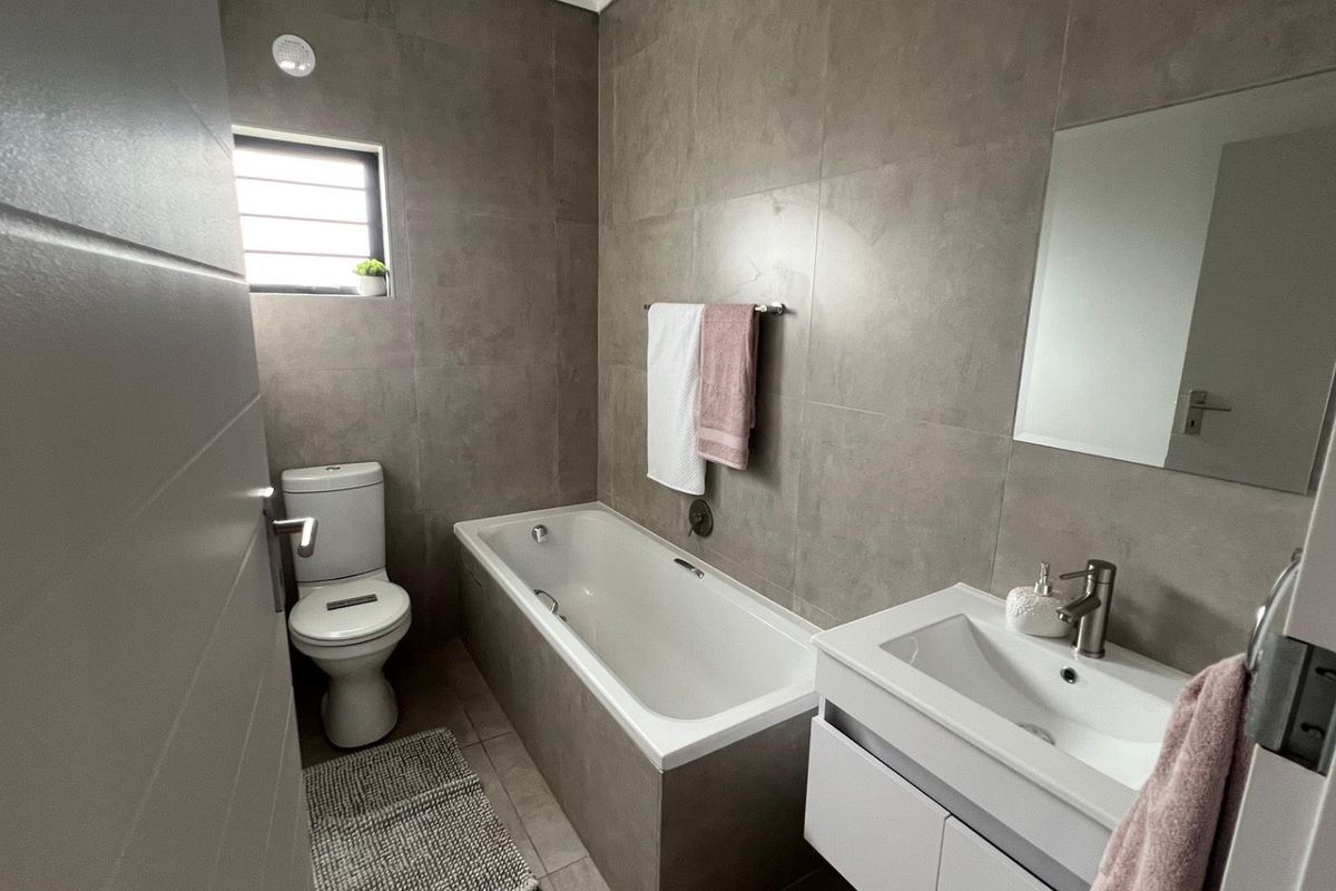 Modern bathroom featuring large format grey wall tiles, a built-in bathtub, a wall-mounted vanity with basin, and a toilet.