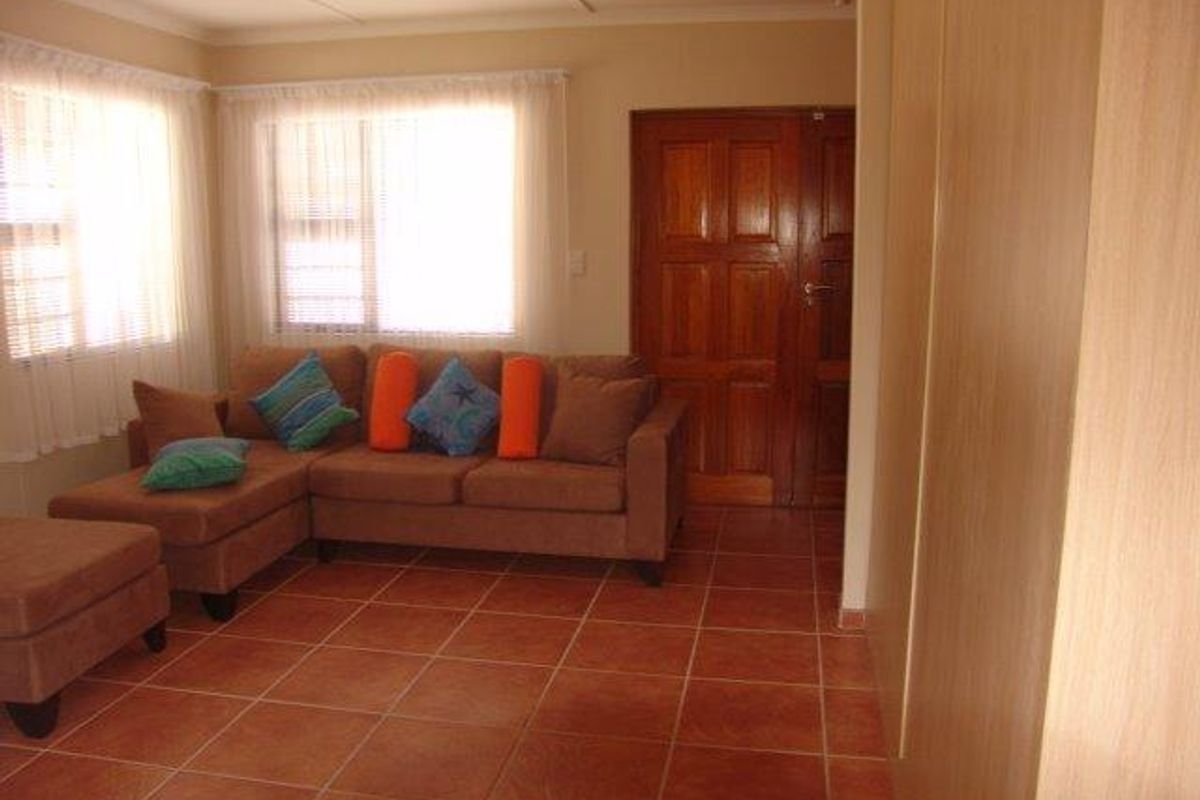 A living room featuring terracotta floor tiles, built-in cabinetry, and a solid timber door, offering a functional and traditional living space.