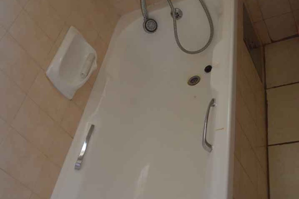 A dated bathroom featuring a standard bathtub with a shower mixer, tiled walls and flooring, and a built-in recessed wall niche.
