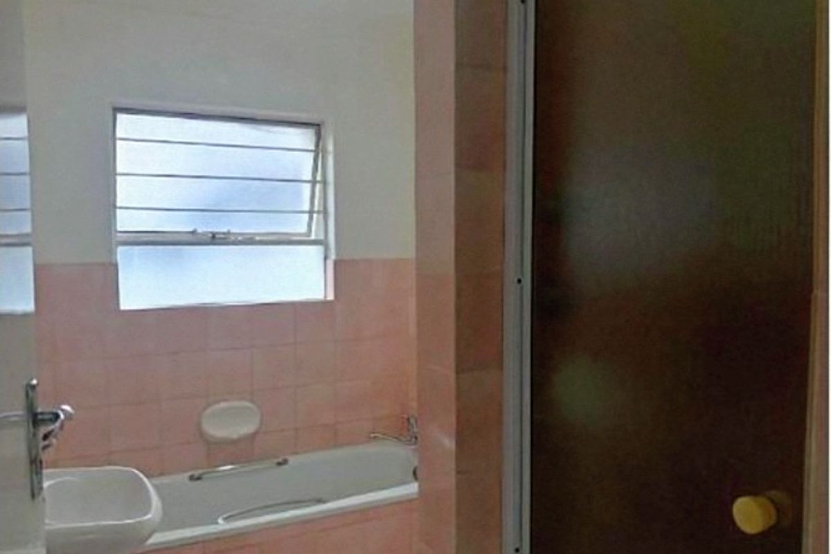 A dated bathroom featuring a bathtub, pedestal basin, and shower enclosure with pink wall tiling and a louvered window.