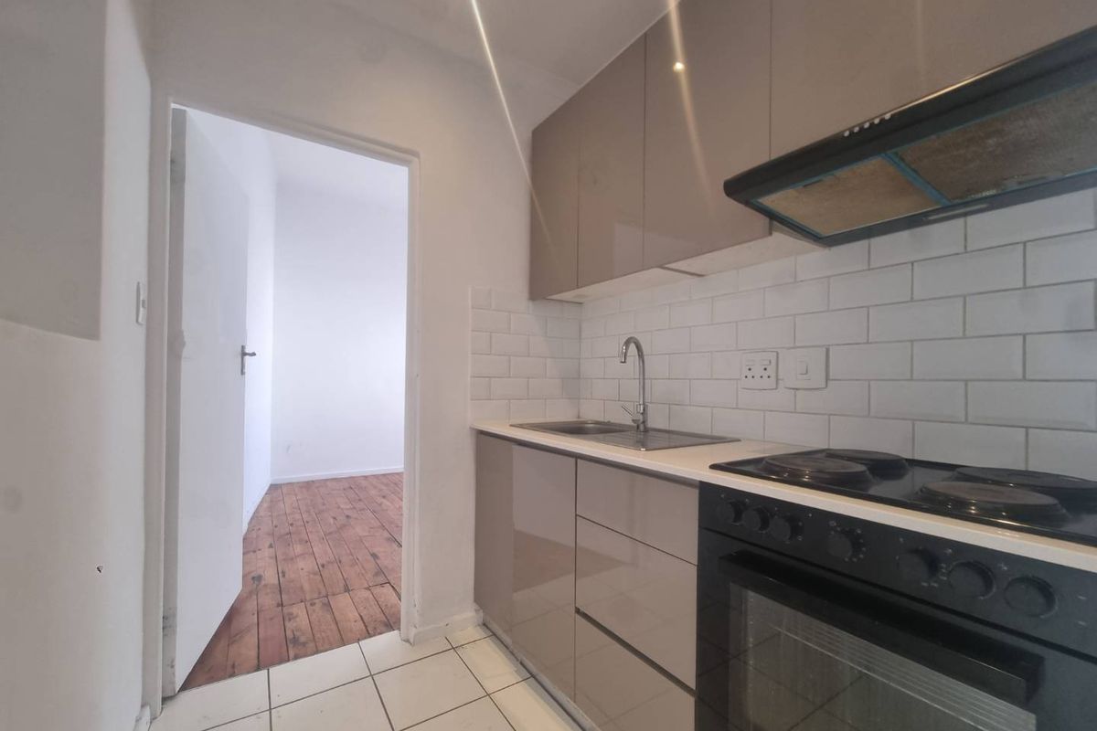 Compact kitchen featuring modern high-gloss cabinetry, subway tile backsplash, integrated oven, and hob, leading into an adjacent room with timber flooring.