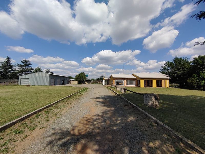 Wide-angle view of the property entrance featuring a long gravel driveway, a large metal outbuilding, and the main residence with surrounding grounds.