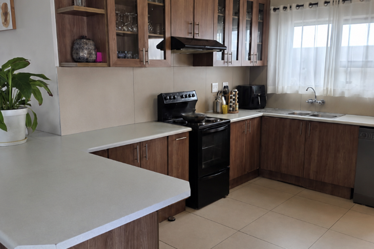 A functional kitchen featuring wood-look cabinetry, laminate countertops, a freestanding stove with extractor fan, and tiled flooring with ample workspace.