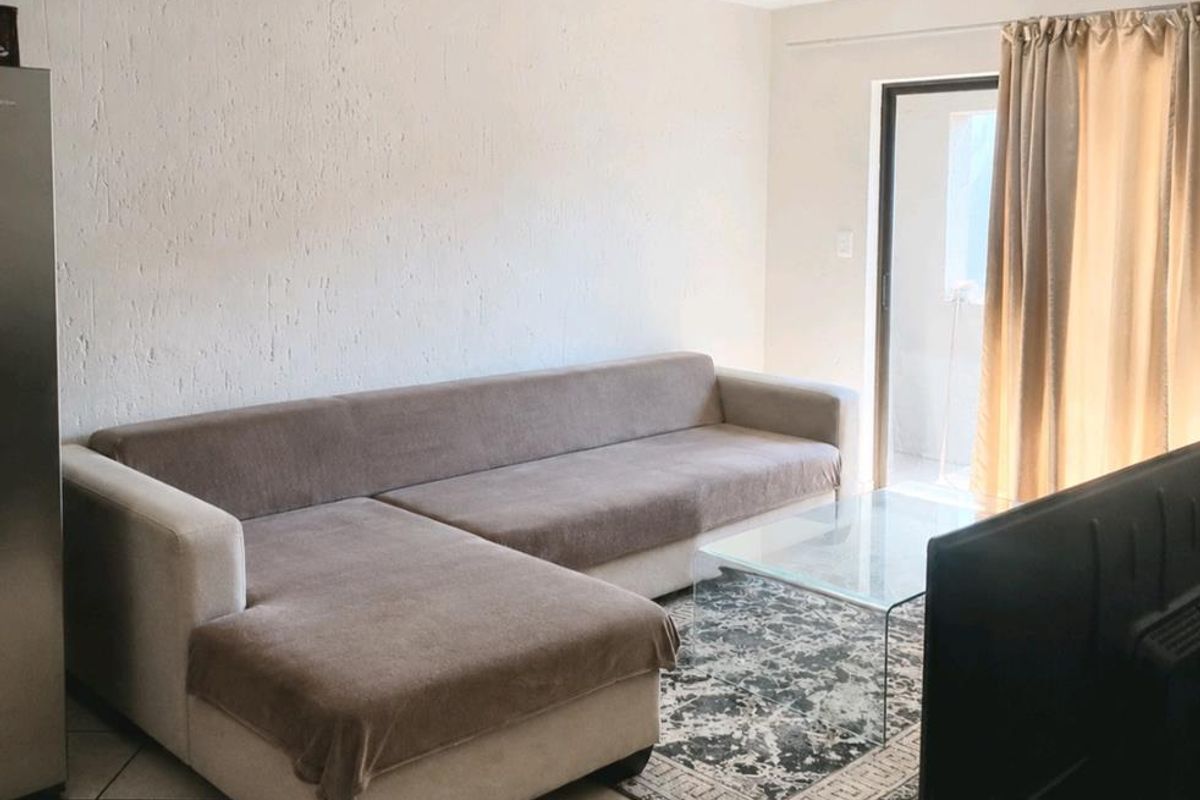 A living room featuring ceramic floor tiles, a sliding glass door providing natural light, and a neutral wall finish.