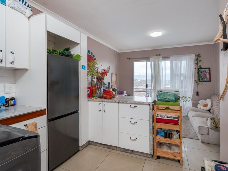 Open-plan kitchen and living area featuring white cabinetry, stone countertops, tiled flooring, and a sliding glass door leading to a balcony.
