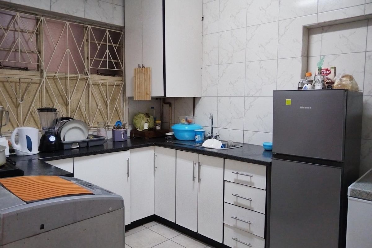 A functional kitchen featuring white cabinetry, dark countertops, tiled backsplash, and tiled flooring, equipped with essential sink and storage space.