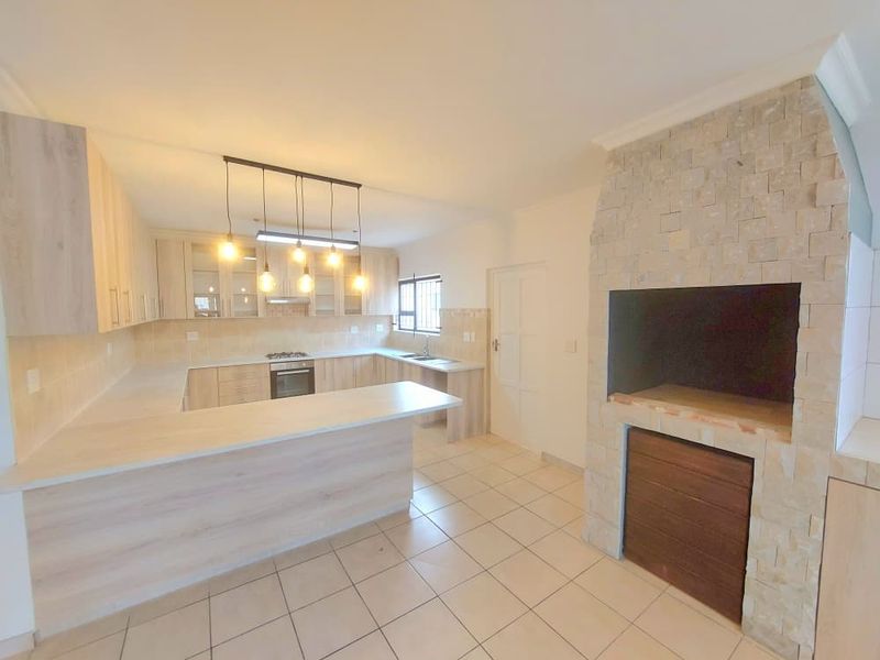 Modern kitchen featuring light wood cabinetry, stone-clad fireplace, breakfast bar, and built-in appliances, offering a clean and functional layout.