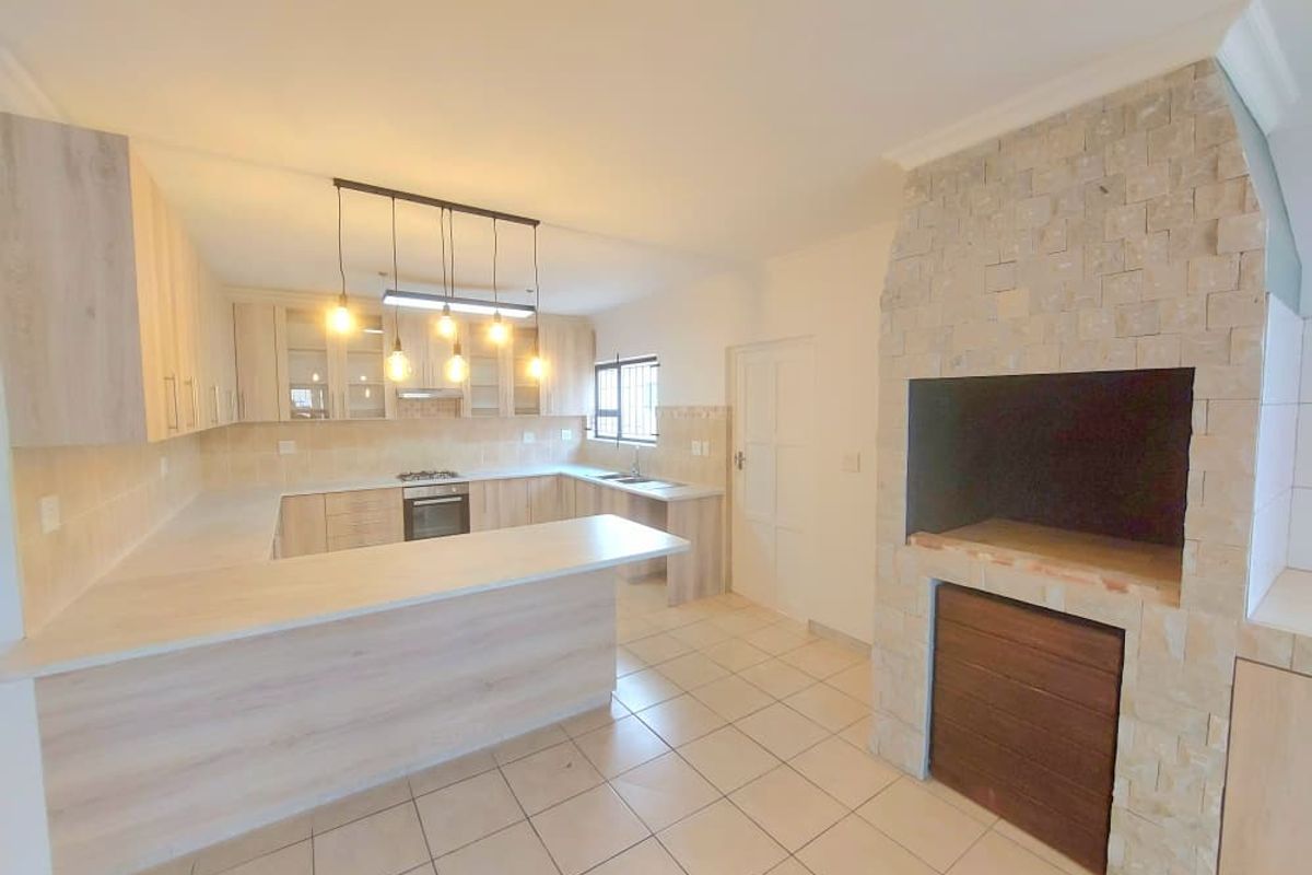 Modern kitchen featuring light wood cabinetry, stone-clad fireplace, breakfast bar, and built-in appliances, offering a clean and functional layout.