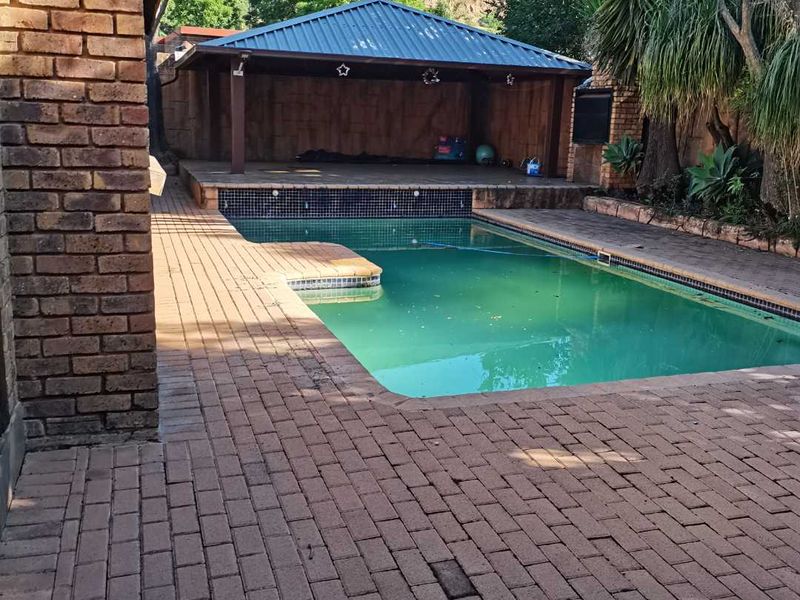 Outdoor pool area featuring a swimming pool, brick paving, and a covered patio with a built-in braai.