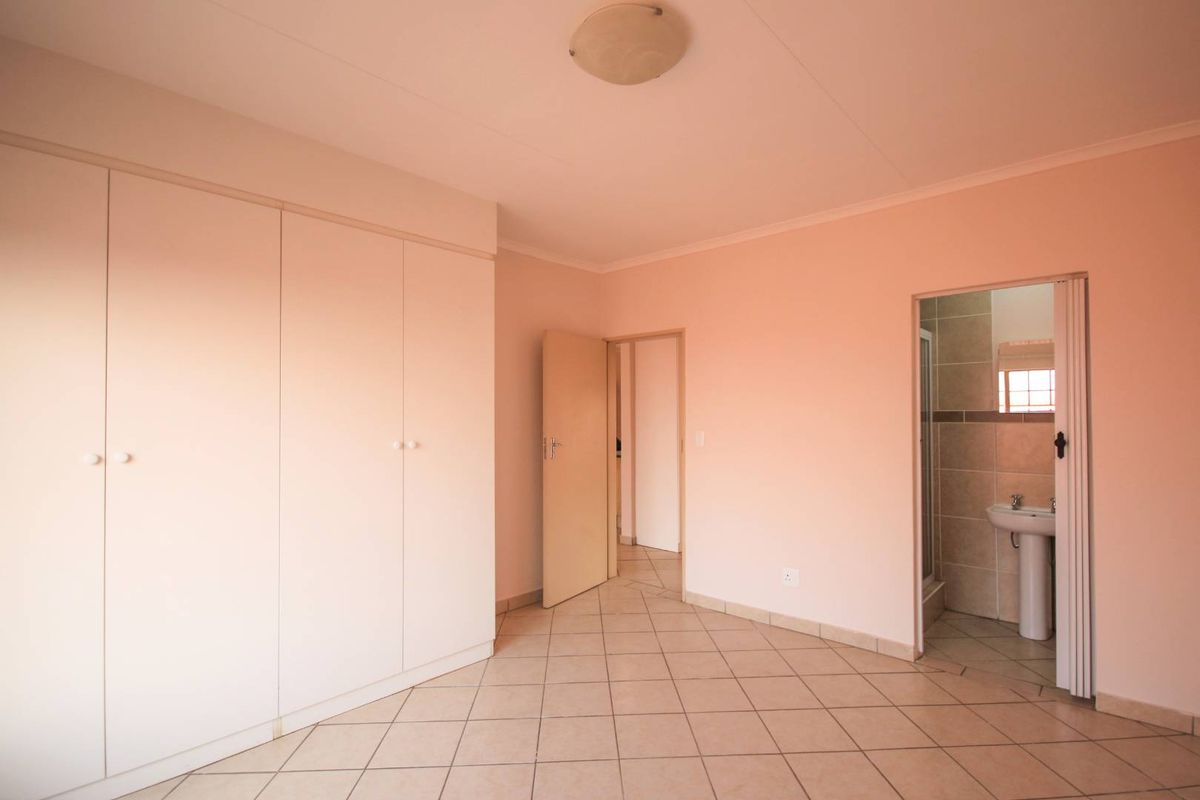 A spacious bedroom featuring built-in cupboards, tiled flooring, and an en-suite bathroom with a shower and pedestal basin.
