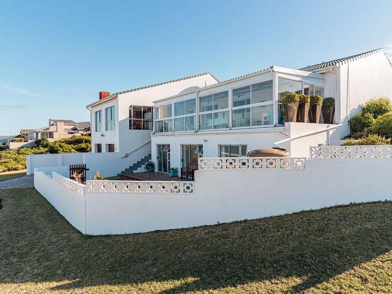 Rear view of the property featuring a white facade, an enclosed upper-level balcony, a paved patio area, and a surrounding concrete boundary wall.