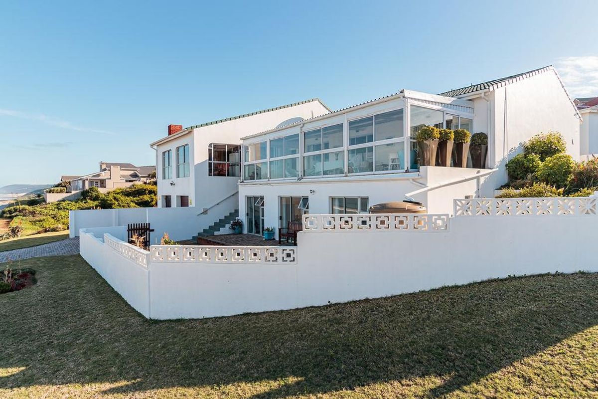Rear view of the property featuring a white facade, an enclosed upper-level balcony, a paved patio area, and a surrounding concrete boundary wall.