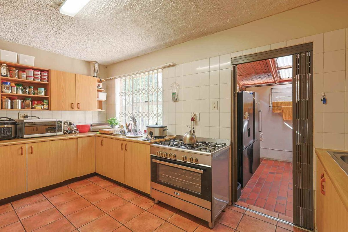 A functional kitchen featuring light wood cabinetry, tiled splashbacks, a gas stove, and direct access to an adjacent utility area.