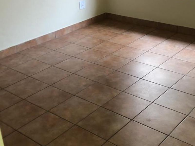 An empty bedroom featuring neutral walls, ceramic floor tiles, and a window fitted with security burglar bars.