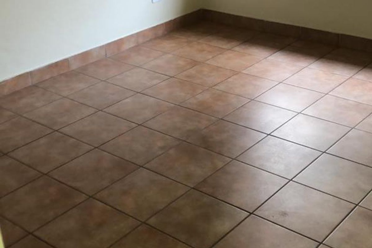 An empty bedroom featuring neutral walls, ceramic floor tiles, and a window fitted with security burglar bars.