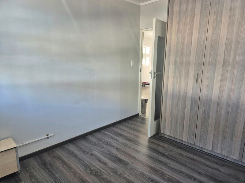A clean, empty bedroom featuring modern wood-look laminate flooring and built-in cupboards, offering a neutral space ready for personalization.