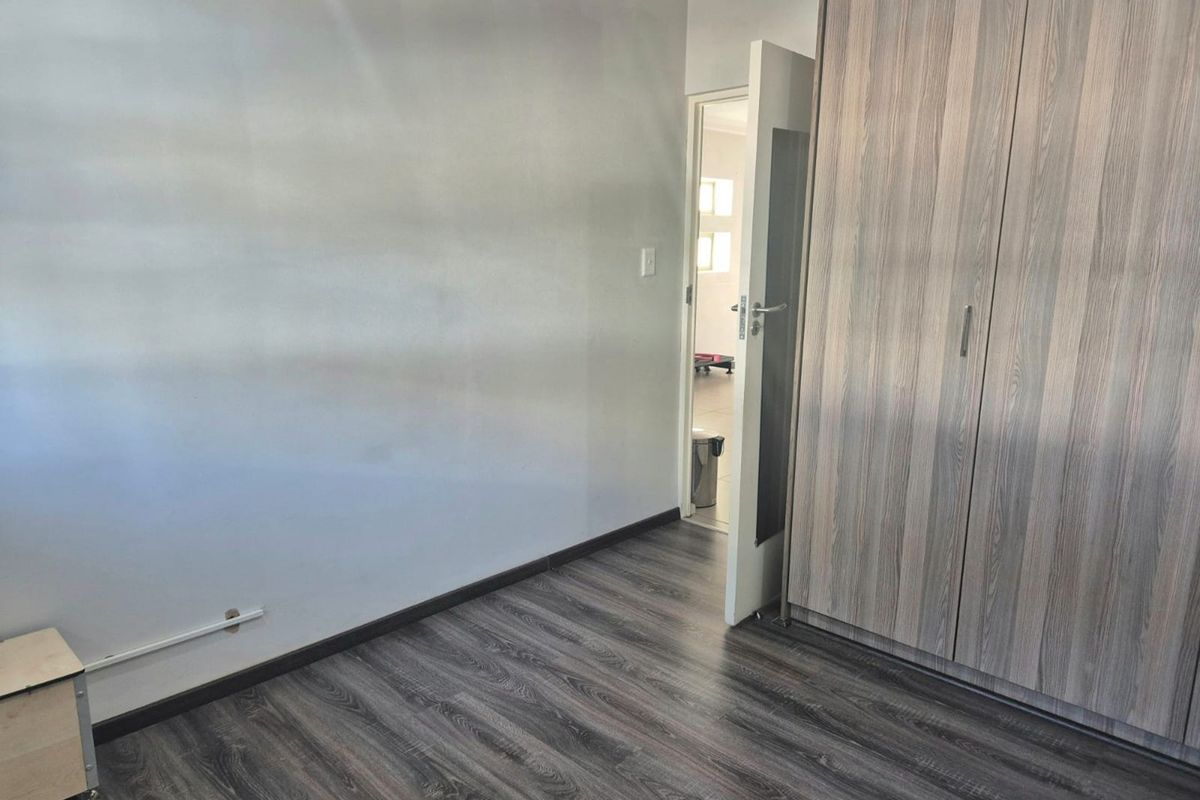 A clean, empty bedroom featuring modern wood-look laminate flooring and built-in cupboards, offering a neutral space ready for personalization.