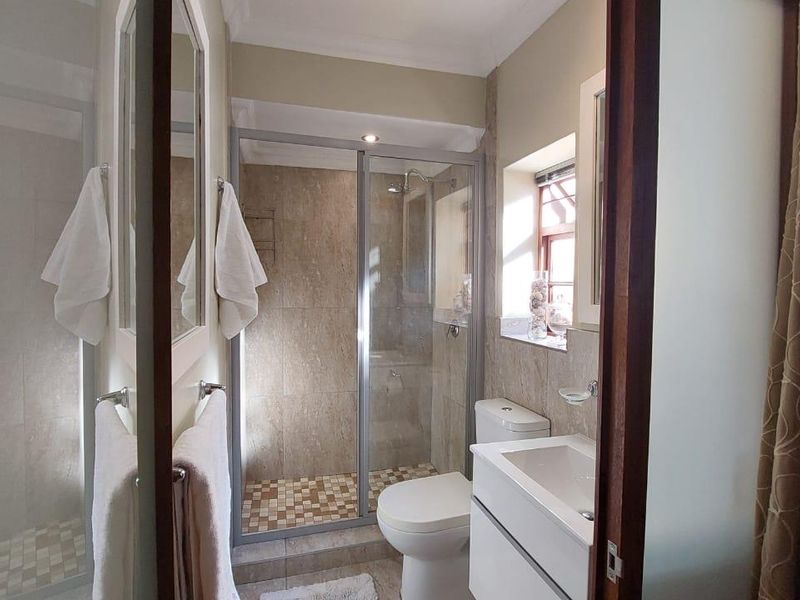 A well-maintained bathroom featuring a glass-enclosed shower, modern wall-mounted vanity with basin, and neutral wall tiling.