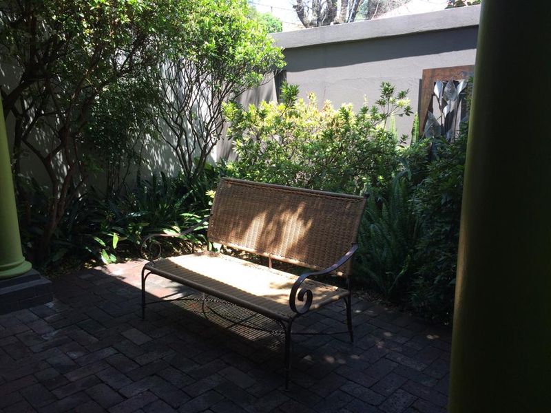 A private, paved patio area enclosed by a boundary wall and surrounded by established garden greenery, offering a quiet outdoor retreat.
