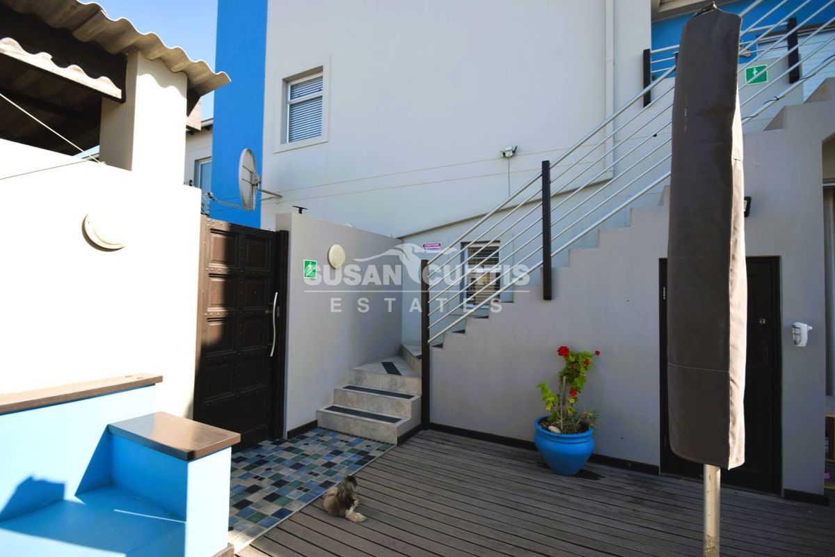 Exterior view of a multi-level outdoor area featuring a wooden deck, external staircase with metal railings, and a tiled entrance landing.