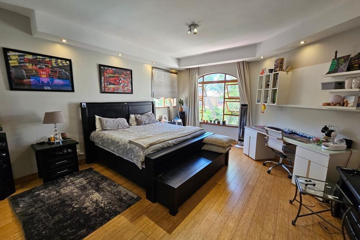 Spacious bedroom featuring warm timber flooring, recessed ceiling lighting, and a large arched window providing natural light and garden views.