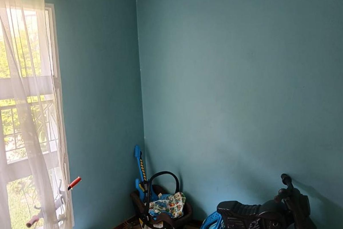 A bedroom featuring tiled flooring, a ceiling fan, and a security gate on the window, providing a functional space with potential for cosmetic updates.