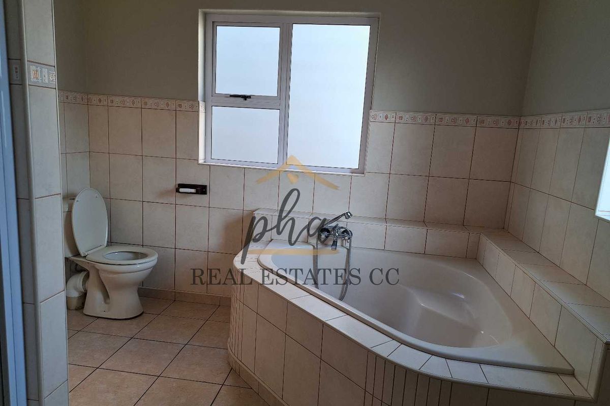 A functional bathroom featuring a built-in corner bathtub, a toilet, and neutral wall and floor tiling.