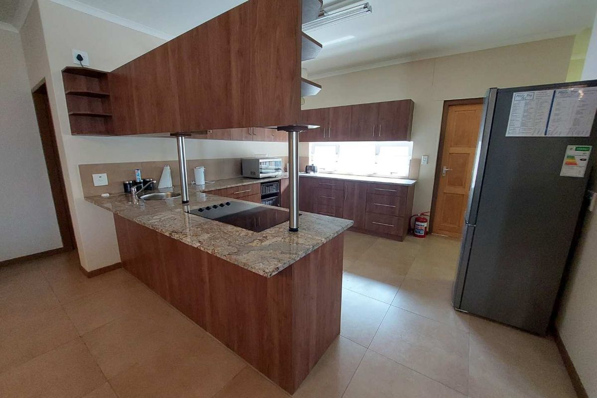 A functional kitchen featuring wood-finish cabinetry, granite countertops, a central breakfast bar with an integrated hob, and tiled flooring.