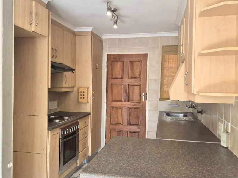 A functional kitchen featuring light wood cabinetry, laminate countertops, built-in oven with hob, and a tiled backsplash, offering a clean and practical workspace.