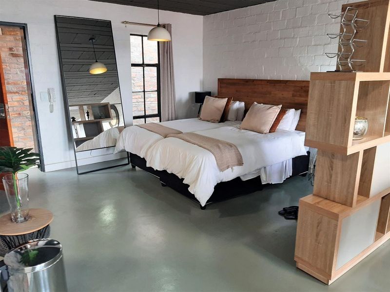 A spacious bedroom featuring polished concrete flooring, exposed brick accents, and a custom timber headboard, creating a modern industrial aesthetic.