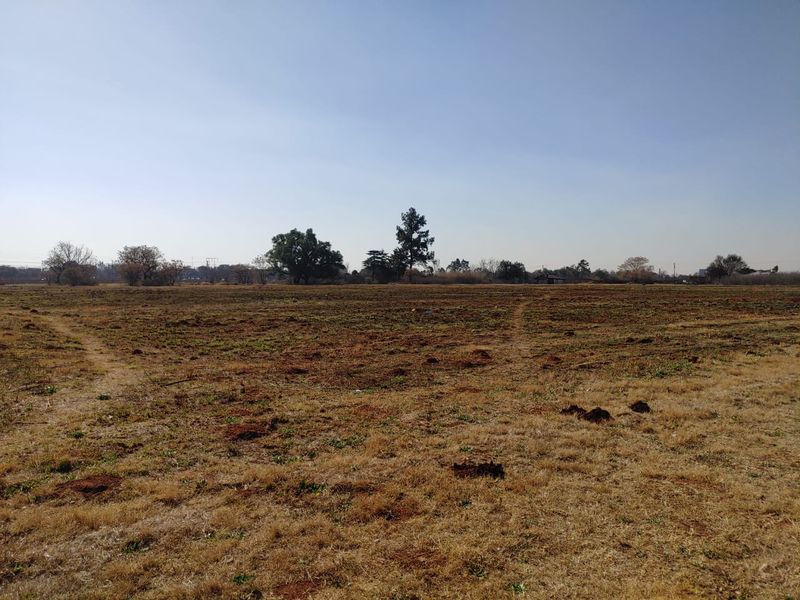 A wide-angle view of a large, flat, undeveloped commercial land plot with sparse vegetation and clear horizon.