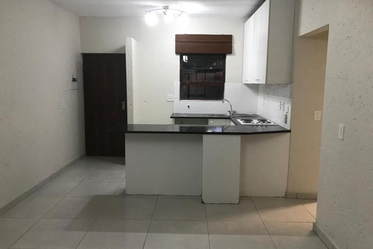 A functional, empty kitchen featuring white cabinetry, granite countertops, an electric hob, and tiled flooring, ready for personalization or staging.