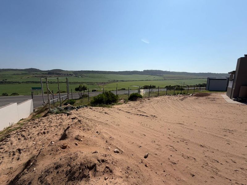 An elevated view overlooking open fields and a distant landscape, featuring a sandy foreground and perimeter fencing.