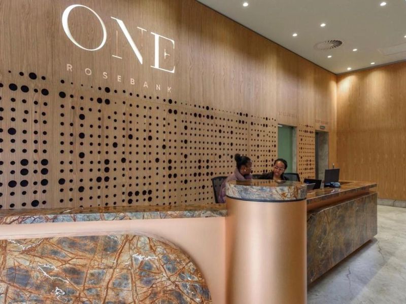 Modern reception area featuring a stone-topped desk, decorative wood paneling with integrated branding, and professional recessed lighting.