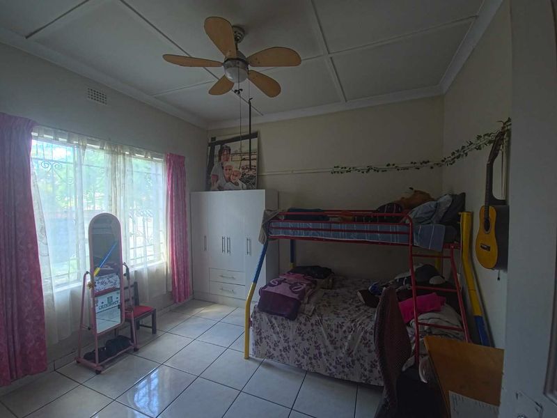 A bedroom featuring tiled flooring, a ceiling fan, and a built-in wardrobe, with security bars installed on the windows.