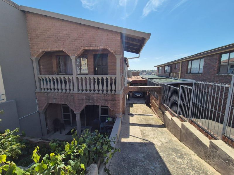 Rear view of a multi-level face brick house featuring a balcony with balustrades, a concrete driveway, and a covered carport area.