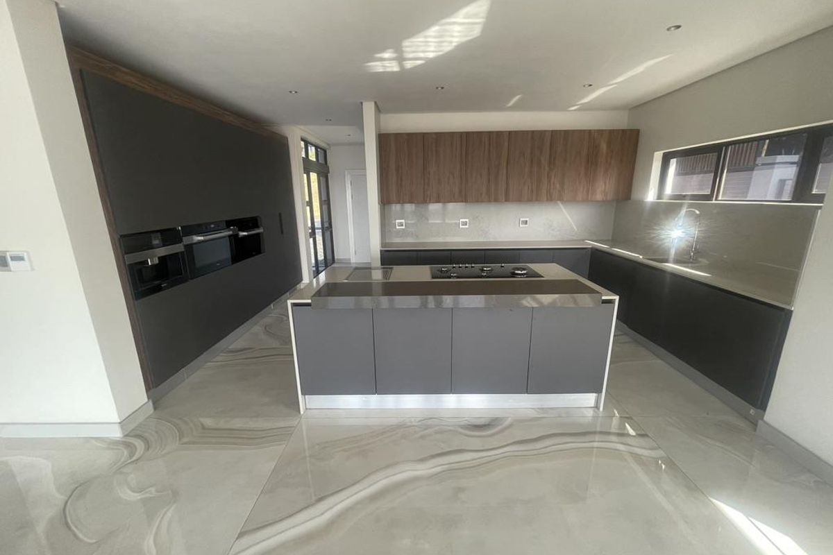 Modern kitchen featuring sleek dark cabinetry, a central island with a built-in cooktop, stone countertops, and polished marble-effect flooring.
