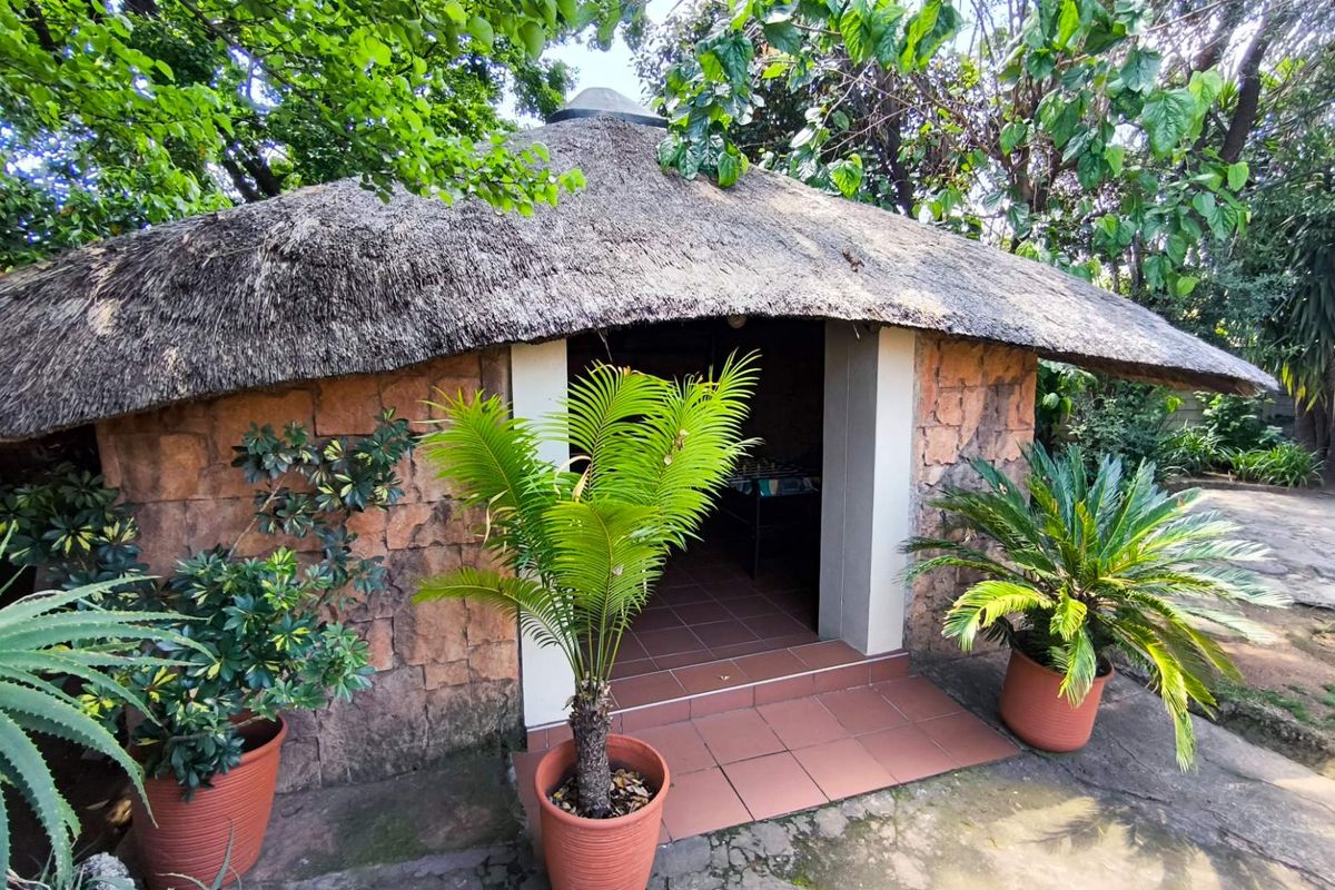 A rustic outdoor structure featuring traditional stone cladding and a thatched roof, set within a landscaped garden area.