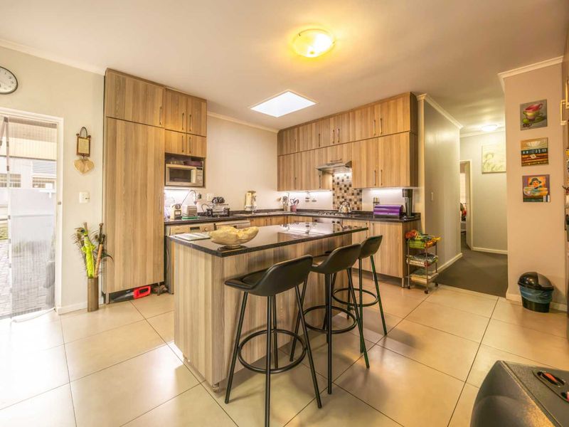 Modern kitchen featuring wood-finish cabinetry, granite countertops, a central island with breakfast bar seating, and a skylight for natural illumination.