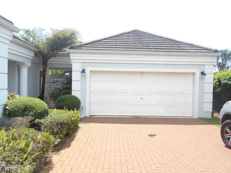 A well-maintained single garage with a white sectional door, complemented by a paved driveway and established garden landscaping.