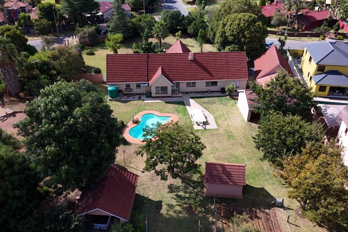 Aerial view of a residential property featuring a large garden, swimming pool, tiled roof house, and multiple outbuildings in a suburban setting.