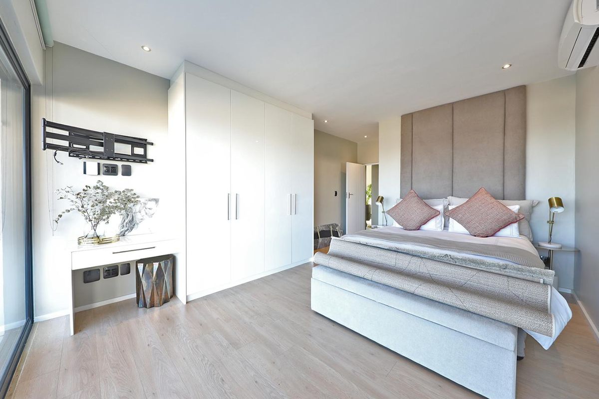 Modern bedroom featuring light wood-look flooring, built-in white cabinetry, a neutral upholstered headboard, and a wall-mounted air conditioning unit.