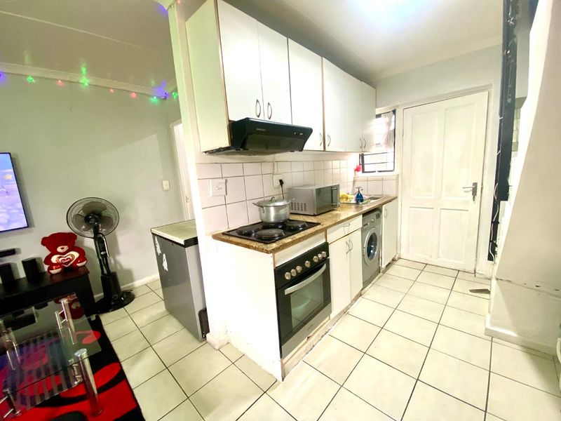 Open-plan kitchen area featuring white cabinetry, built-in oven and hob, and tiled flooring, seamlessly connected to the adjacent living space.